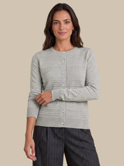 A woman modeling a light gray knit cardigan with button-front closure and textured horizontal ribbing, paired with dark pinstriped trousers, against a solid beige studio background.