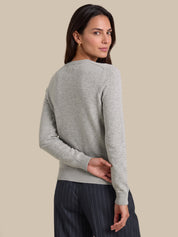 A woman shown from the back wearing a light gray knit sweater and dark pinstriped trousers, photographed against a plain beige studio background.