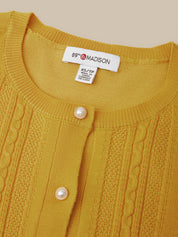 Close-up of a mustard yellow cable-knit cardigan sweater with pearl buttons and a visible neck label reading 89th & Madison.