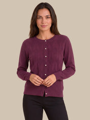 A woman modeling a long-sleeve crewneck cardigan sweater in a deep plum purple color, featuring a button-down front and textured knit pattern, set against a solid beige background.