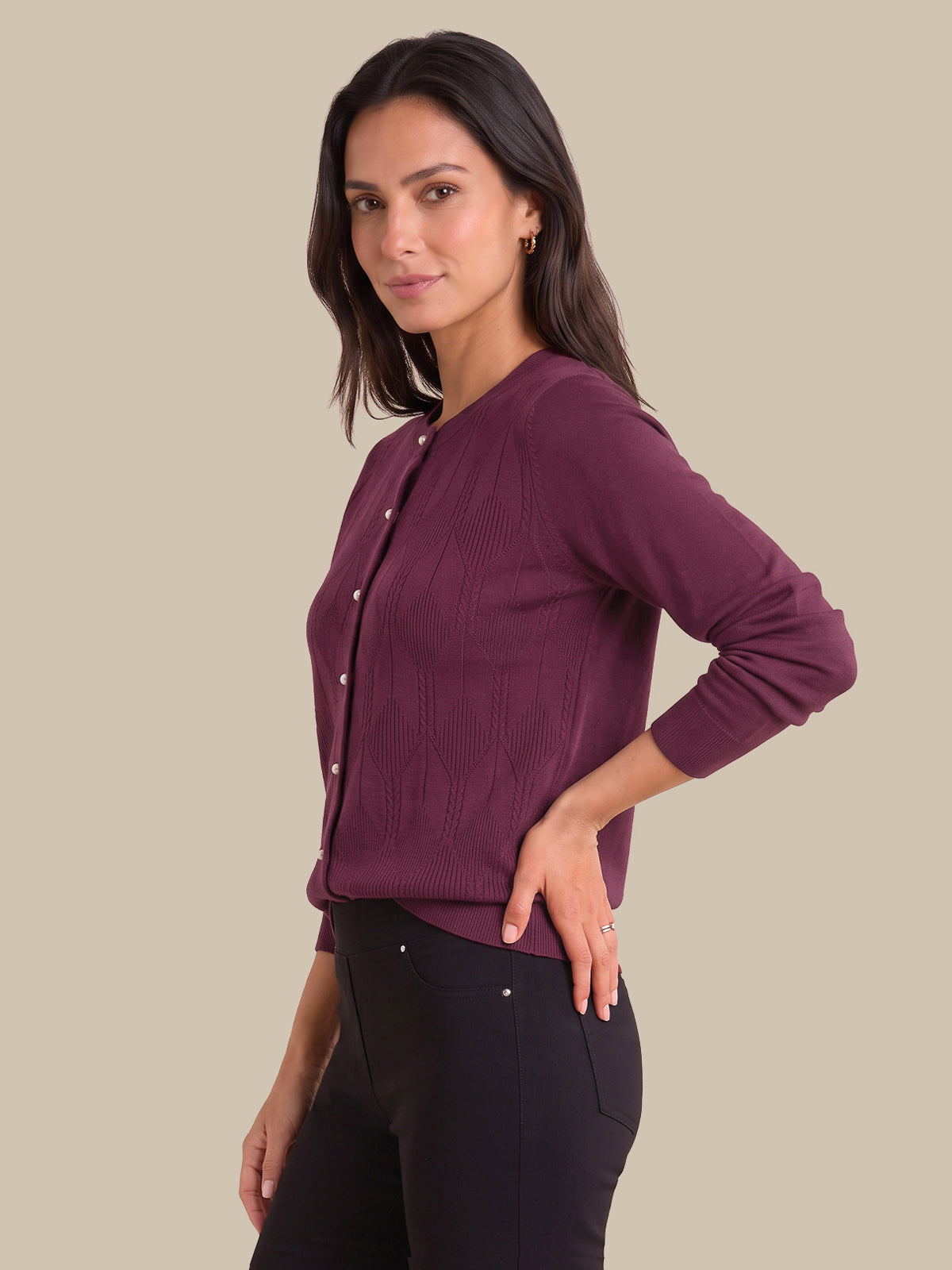 A woman modeling a long-sleeve ribbed knit cardigan in deep plum purple with white buttons, paired with black pants, against a solid beige background.