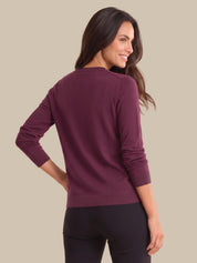 A woman shown from the back wearing a long-sleeve crewneck sweater in a deep plum purple color, paired with black leggings, against a solid beige background.