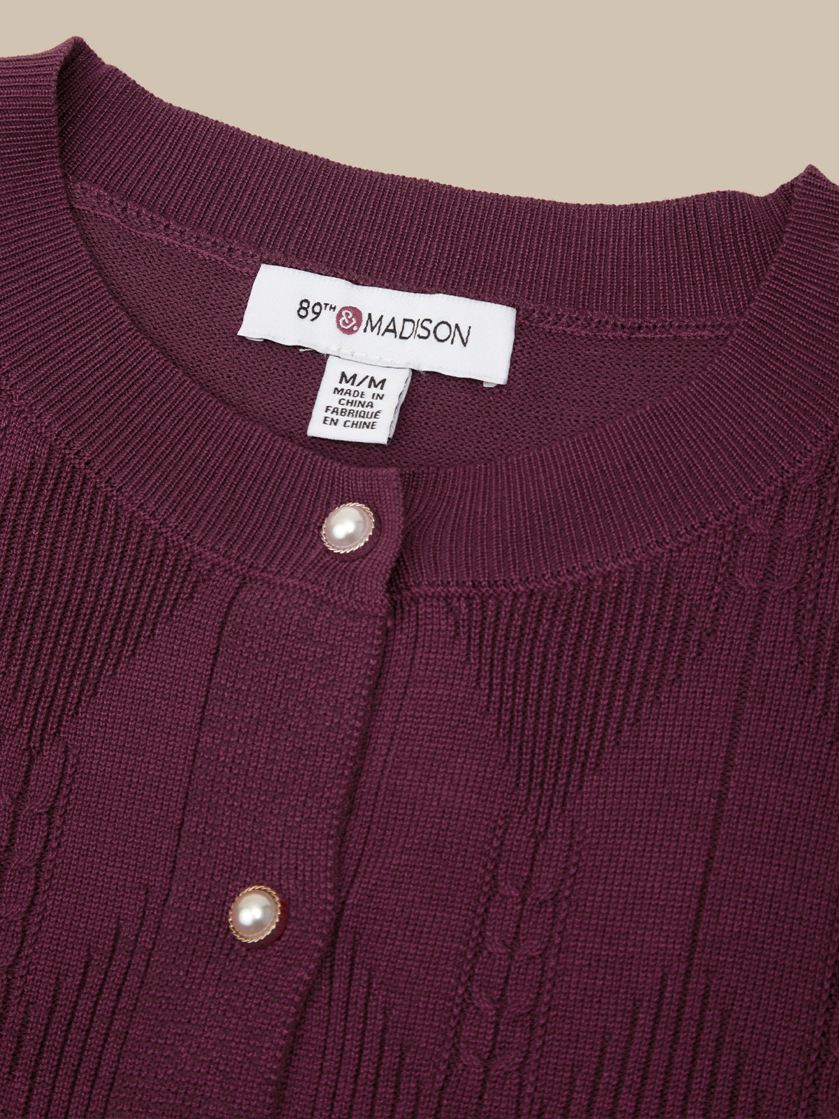 Close-up of a ribbed knit cardigan sweater in deep plum purple, featuring a white button-down collar label reading '89th MADISON' and two pearl-like buttons.