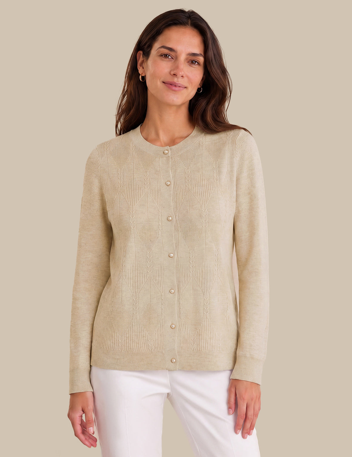 A woman wearing a light beige ribbed knit cardigan sweater with a button-up front, paired with white pants, against a solid beige background.