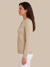 A woman shown in side profile wearing a light beige knit cardigan with white pants, set against a solid beige background.