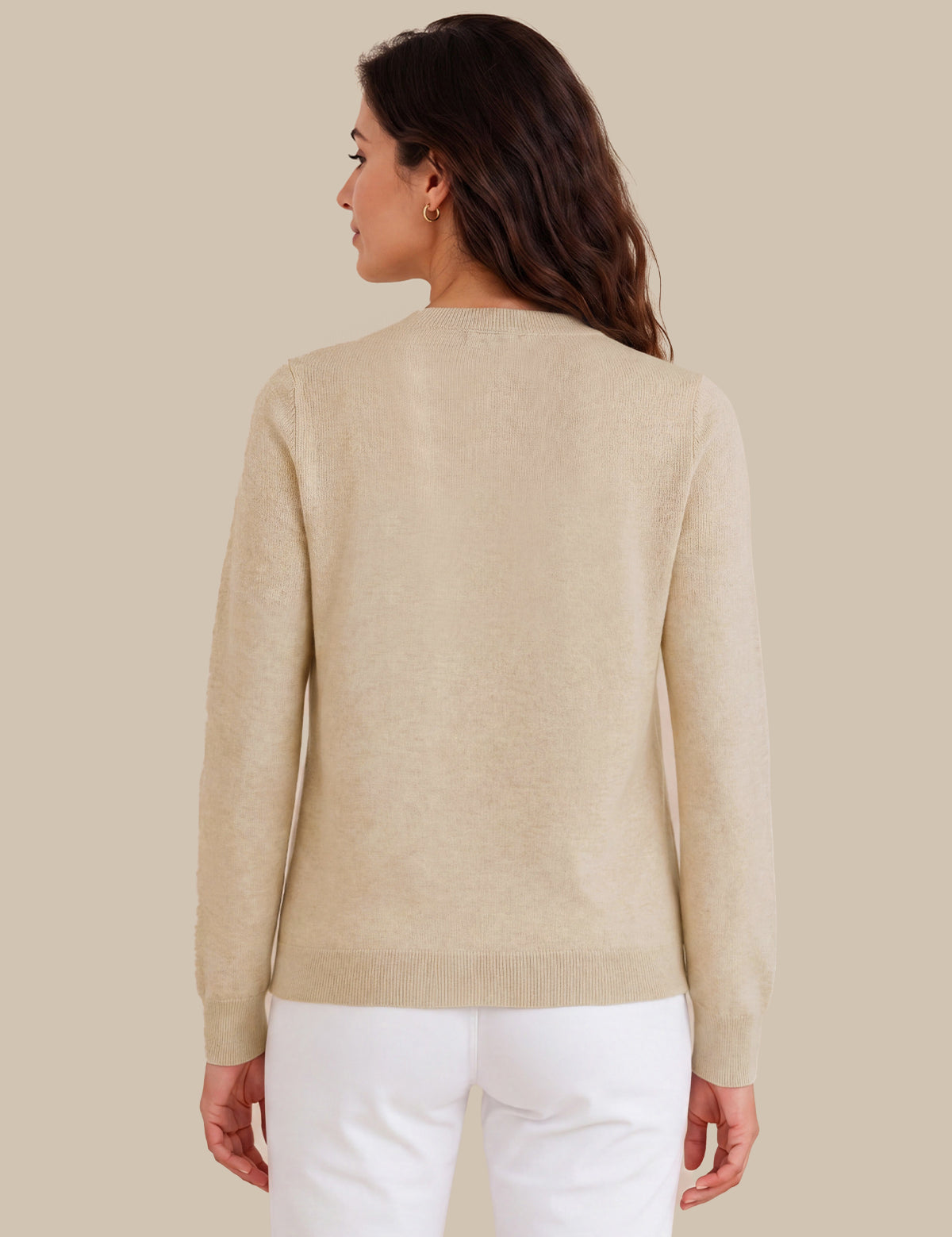 A woman shown from the back wearing a light beige knit sweater and white pants against a solid beige studio background.