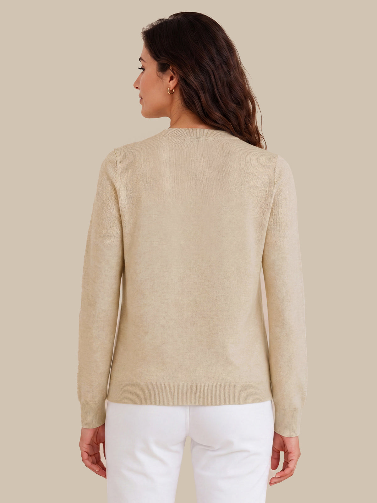 A woman shown from the back wearing a light beige knit sweater and white pants against a solid beige studio background.