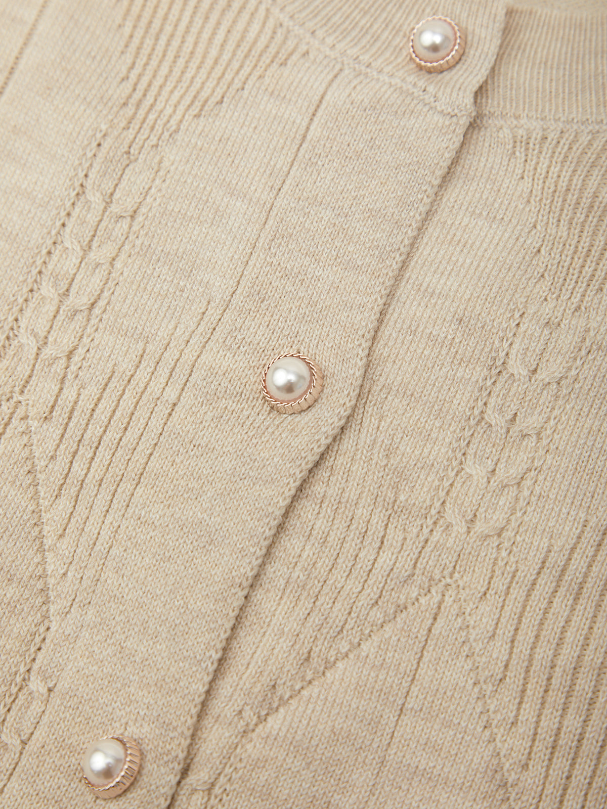 Close-up of a beige ribbed knit cardigan featuring textured cable knit patterns and decorative pearl buttons with metallic rose-gold-toned settings.