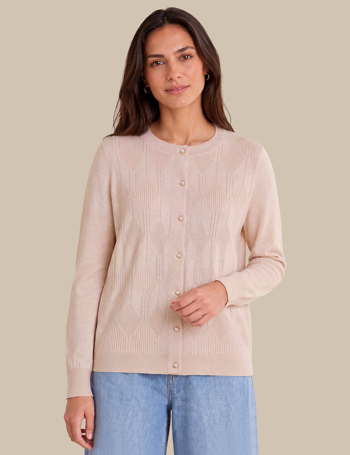 A woman modeling a light pink ribbed knit cardigan with a button-up front, paired with light blue jeans, against a solid beige background.
