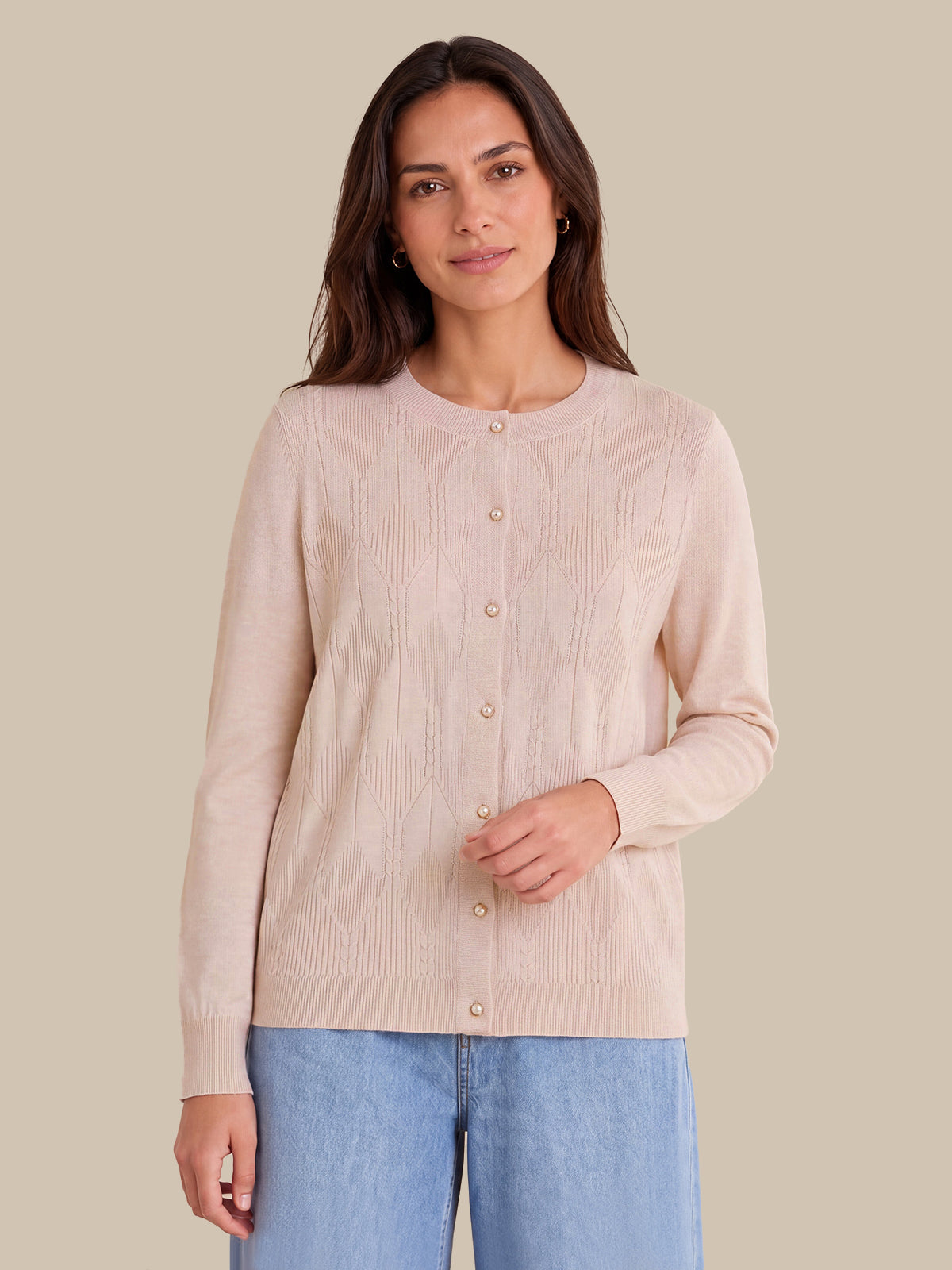 A woman modeling a light pink ribbed knit cardigan with a button-up front, paired with light blue jeans, against a solid beige background.