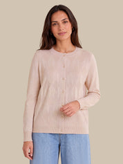 A woman modeling a light pink ribbed knit cardigan with a button-up front, paired with light blue jeans, against a solid beige background.
