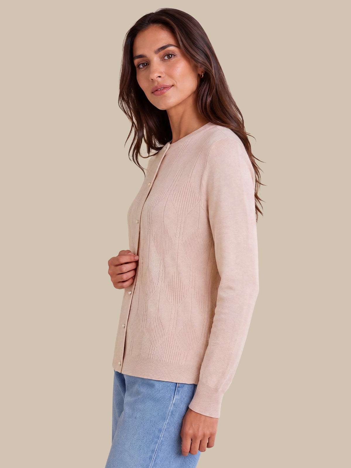 A woman wearing a light pink ribbed knit cardigan sweater and light blue jeans, shown from a side profile against a solid beige background.