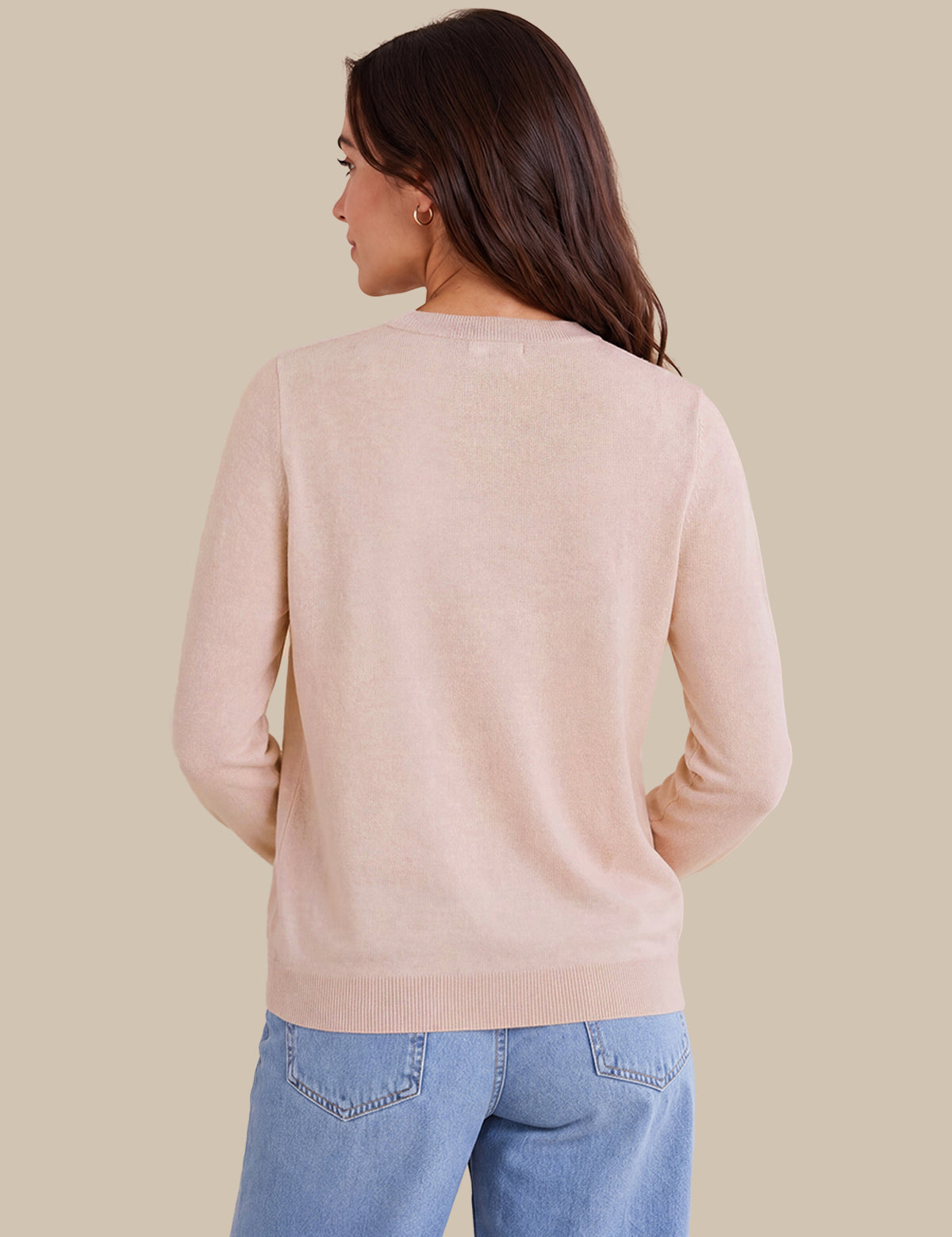 A woman shown from the back wearing a light blush pink knit sweater and light blue jeans against a solid beige background.