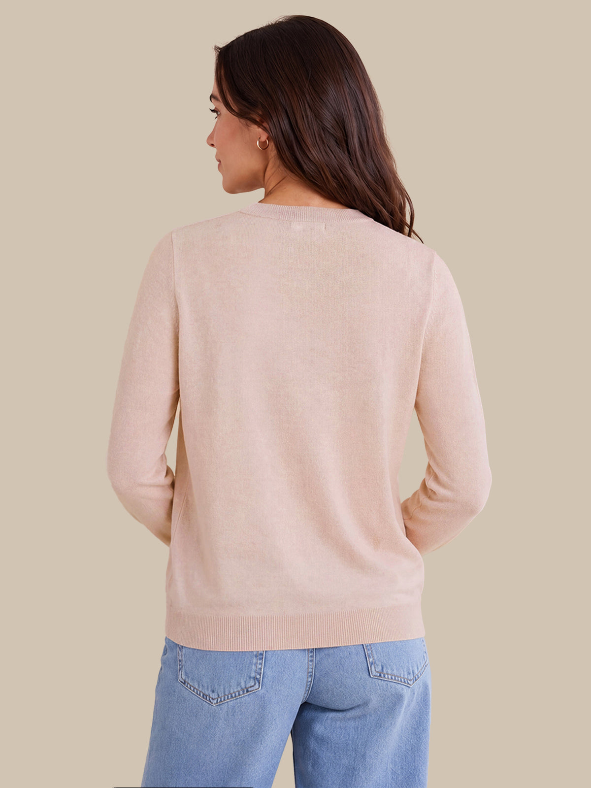 A woman shown from the back wearing a light blush pink knit sweater and light blue jeans against a solid beige background.