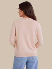A woman shown from the back wearing a light blush pink knit sweater and light blue jeans against a solid beige background.