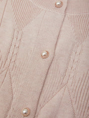 Close-up of a light pink ribbed knit cardigan featuring textured cable and diamond knit patterns, adorned with small pearl-like buttons with rose gold trim.