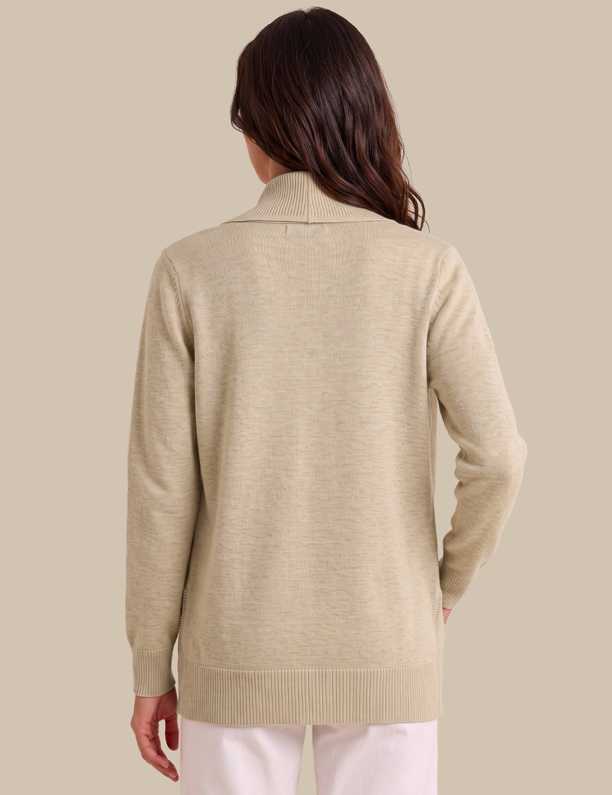 A woman shown from the back wearing a light beige knit sweater with a mock neck and long sleeves, paired with white pants, against a solid beige background.