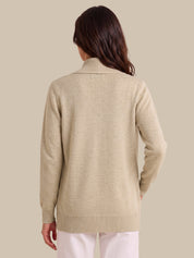 A woman shown from the back wearing a light beige knit sweater with a mock neck and long sleeves, paired with white pants, against a solid beige background.