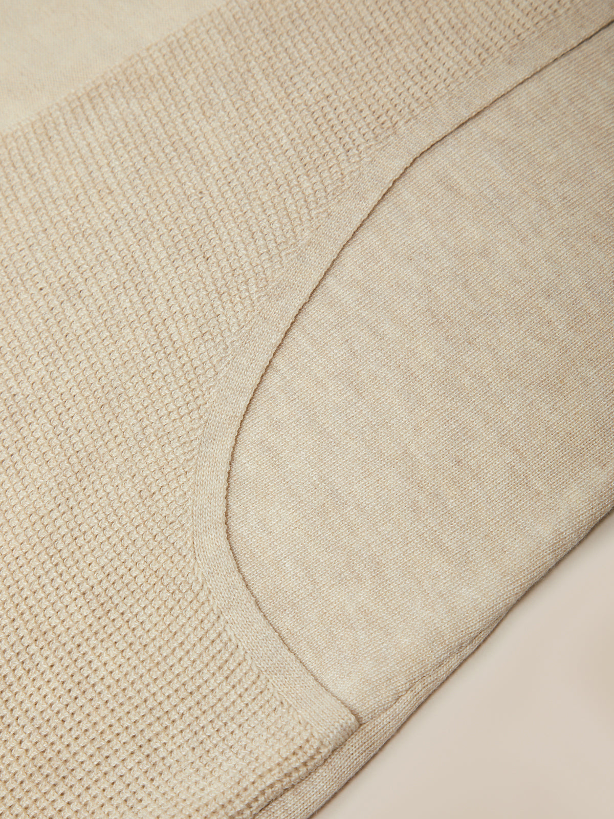 Close-up of a light beige knit fabric with a curved seam and textured knit pattern.