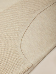 Close-up of a light beige knit fabric with a curved seam and textured knit pattern.