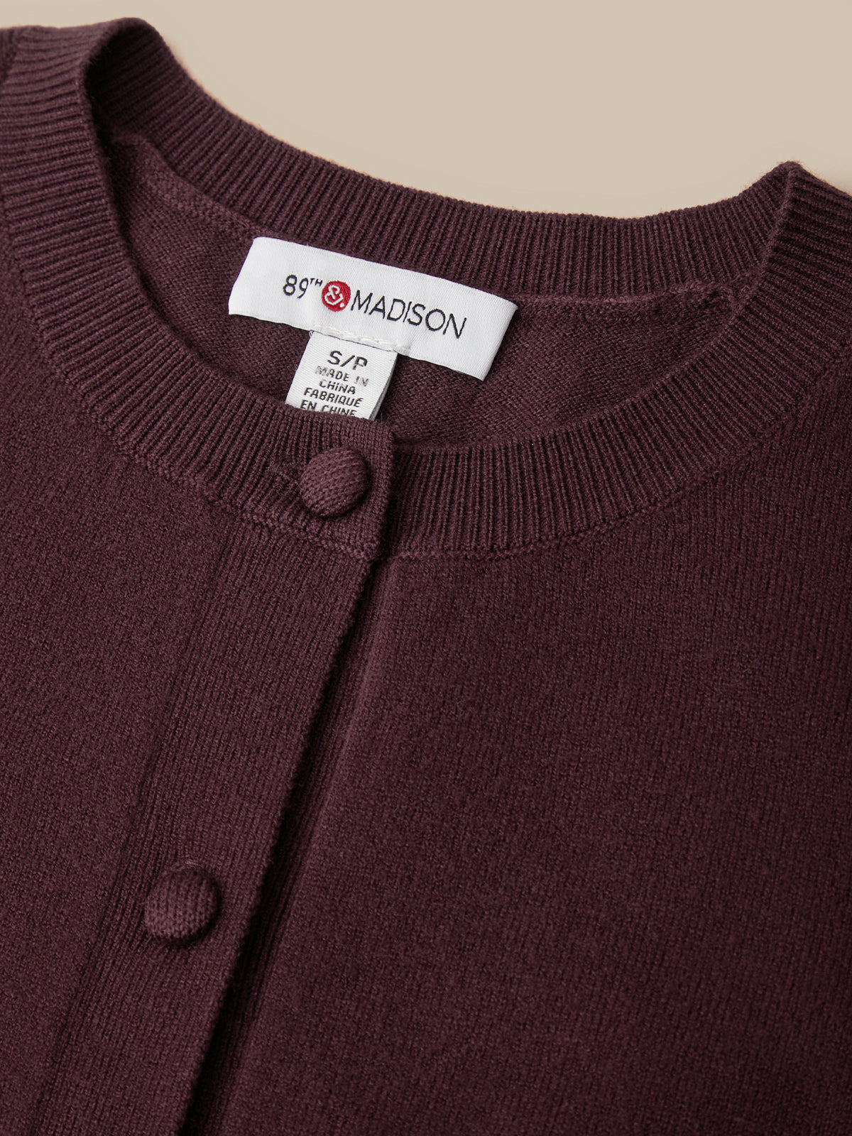 Close-up of a dark burgundy knit cardigan with a button-down front and a visible neck label reading 89th & MADISON.