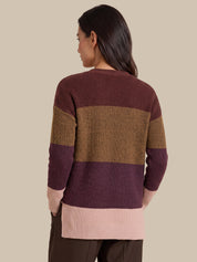 A woman shown from the back wearing a waffle-knit sweater with horizontal color-blocked stripes in dark burgundy, tan, and light pink, paired with dark brown pants against a solid beige background.