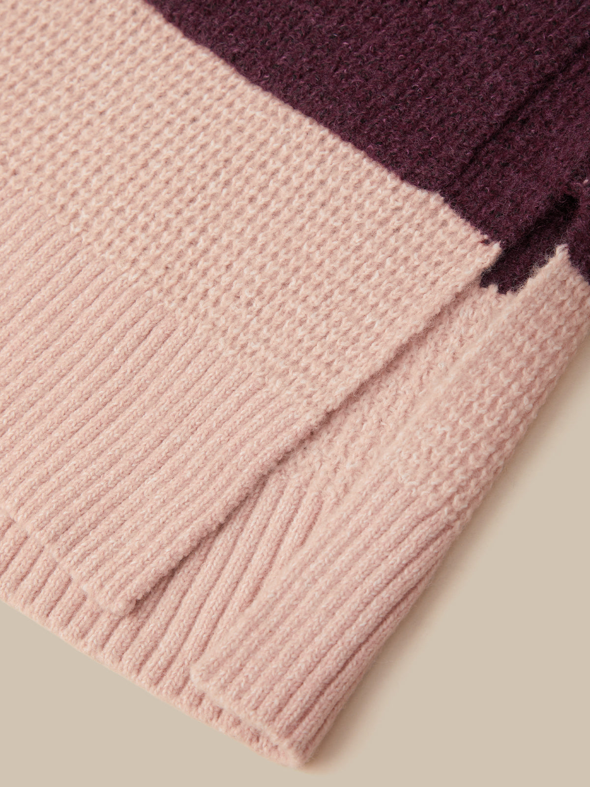 Close-up of a ribbed knit fabric in soft blush pink with a contrasting dark plum purple section, shown on a neutral beige background.