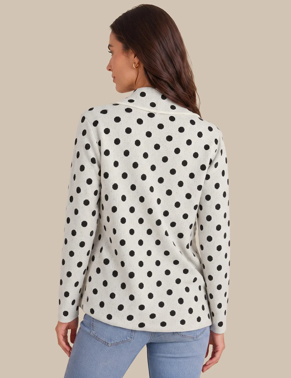 A woman shown from the back wearing a white long-sleeve blazer with a black polka dot pattern, paired with light blue jeans, against a solid beige background.