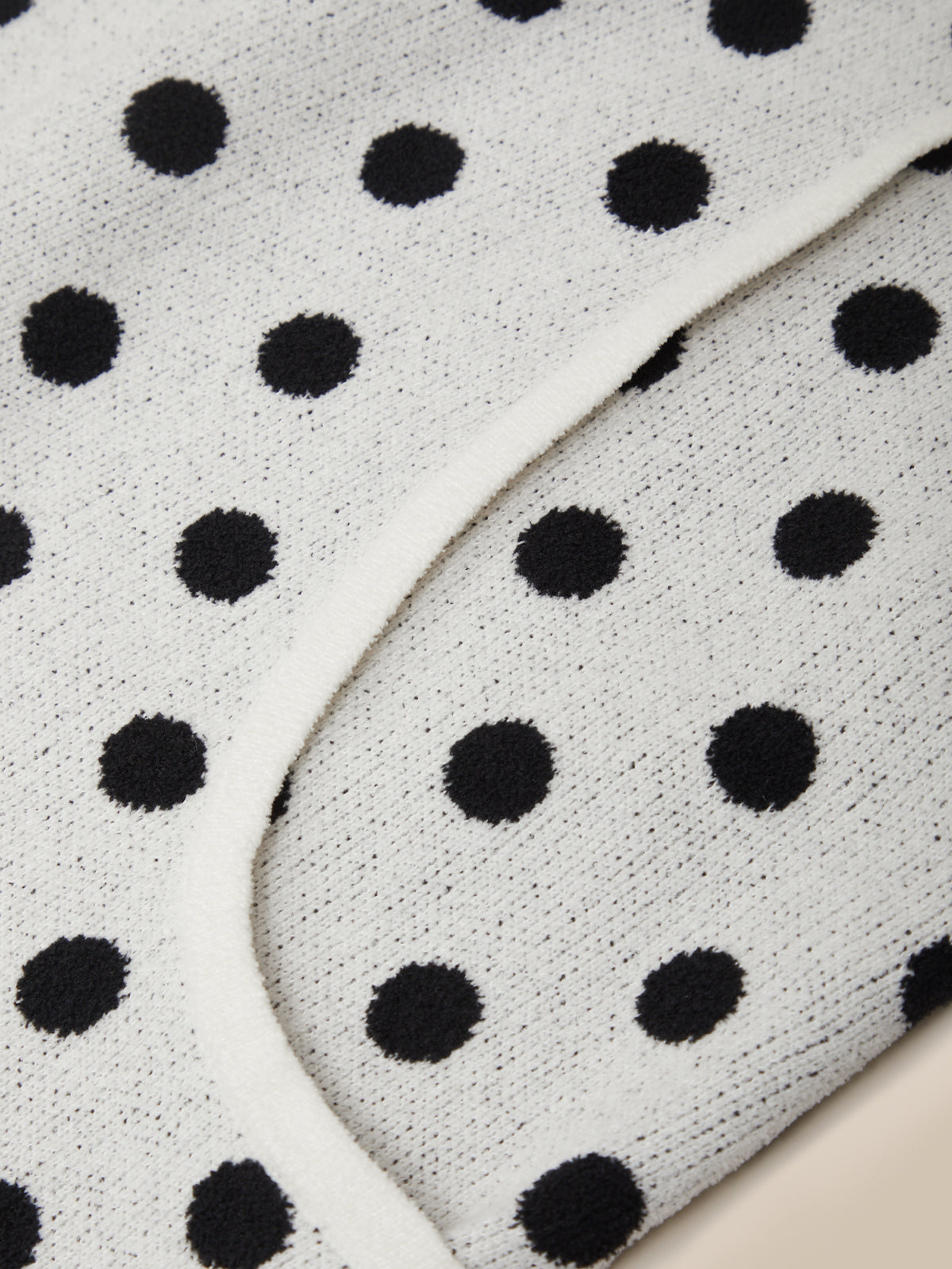Close-up of a white knit fabric with a black polka dot pattern and a curved white trim.