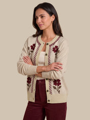A woman modeling a cream-colored knit cardigan with burgundy floral and striped patterns, paired with burgundy pants, against a solid beige background.