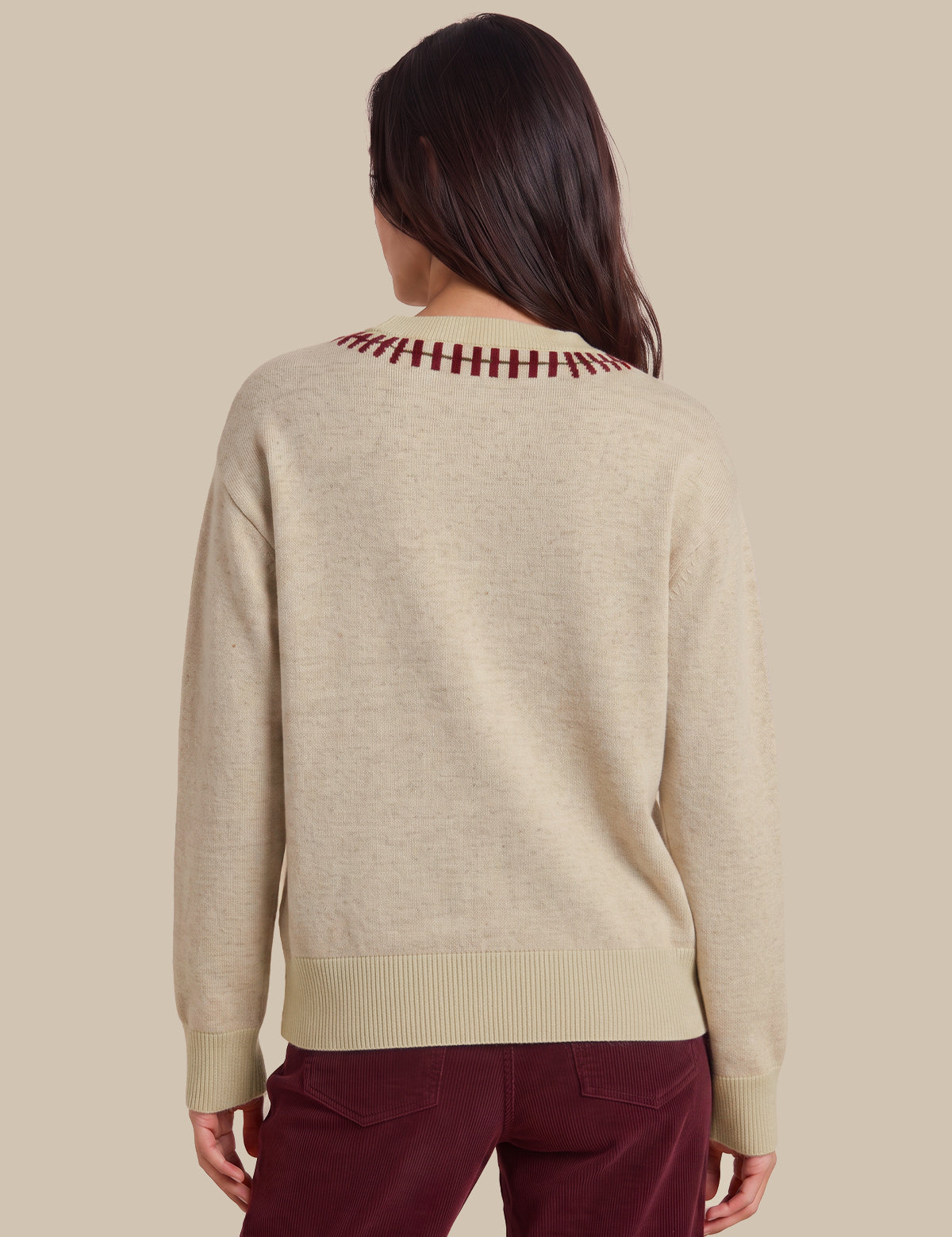 A woman viewed from the back wearing a light beige knit sweater with a burgundy striped crew neck and matching ribbed hem and cuffs, paired with burgundy pants, against a solid beige background.