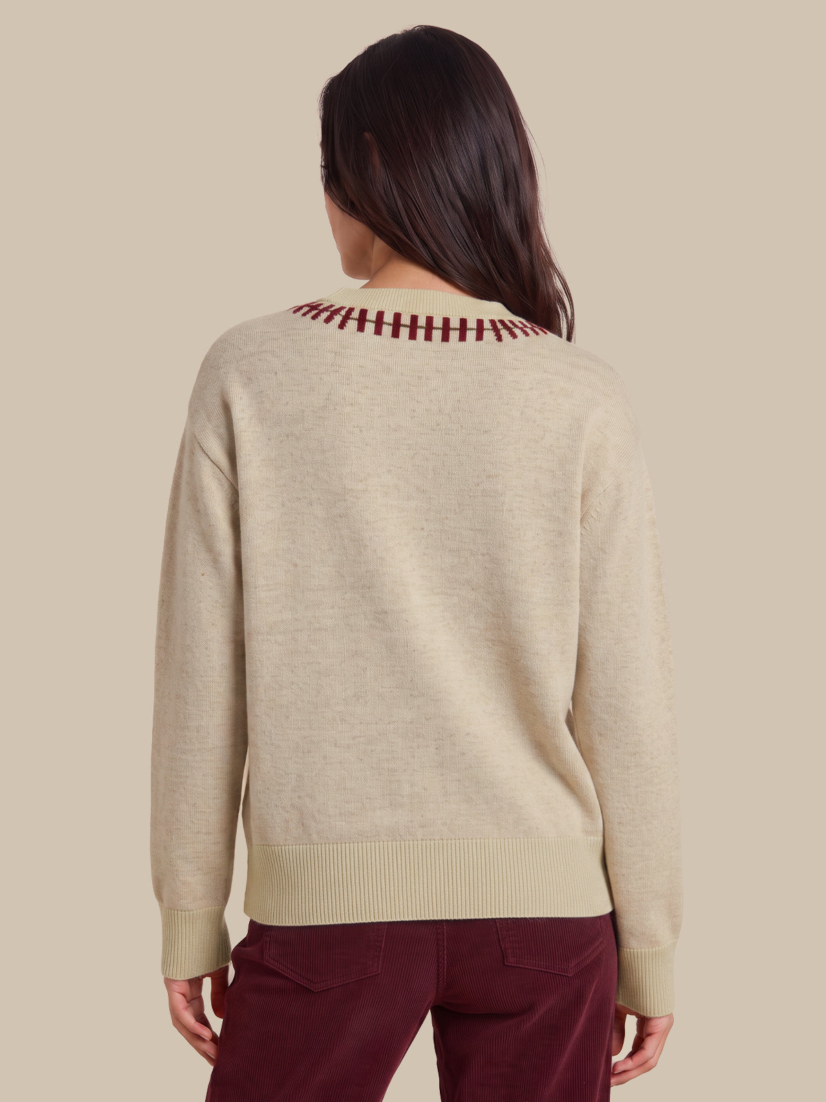 A woman viewed from the back wearing a light beige knit sweater with a burgundy striped crew neck and matching ribbed hem and cuffs, paired with burgundy pants, against a solid beige background.