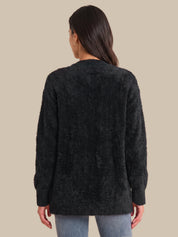 A woman viewed from the back wearing a dark charcoal fuzzy long-sleeve sweater and light blue jeans, set against a solid beige background.