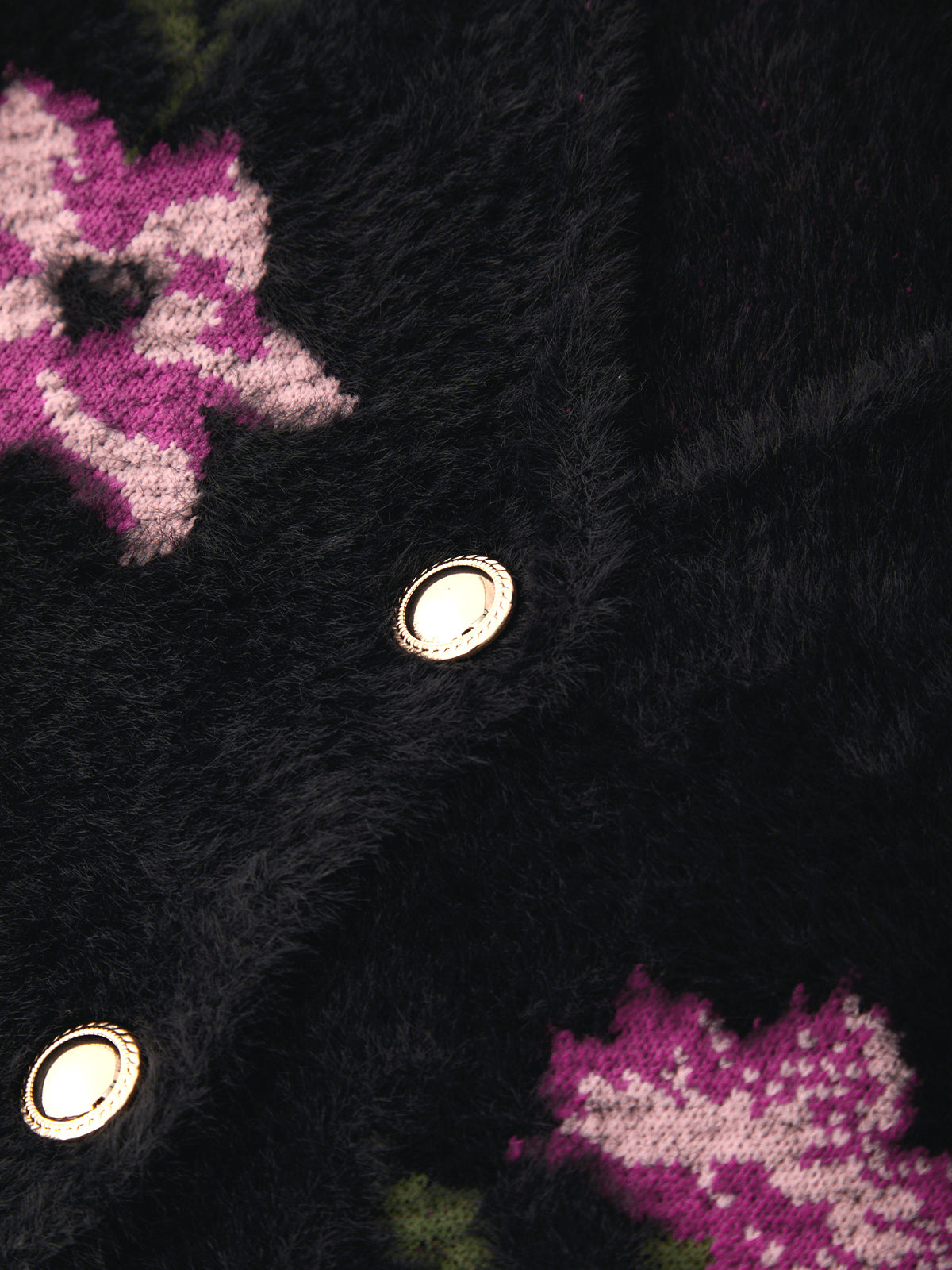 Close-up of a black fuzzy knit garment with pink and white floral patterns and metallic snap buttons.
