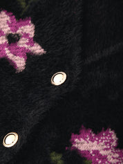 Close-up of a black fuzzy knit garment with pink and white floral patterns and metallic snap buttons.
