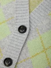 Close-up of a knit cardigan with a gray ribbed V-neck and front opening, featuring black buttons and a light green and yellow argyle pattern.
