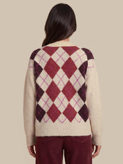 A woman shown from the back wearing a cream-colored knit sweater with a large argyle diamond pattern in burgundy, dark plum, and thin magenta lines, paired with burgundy pants, against a solid beige background.