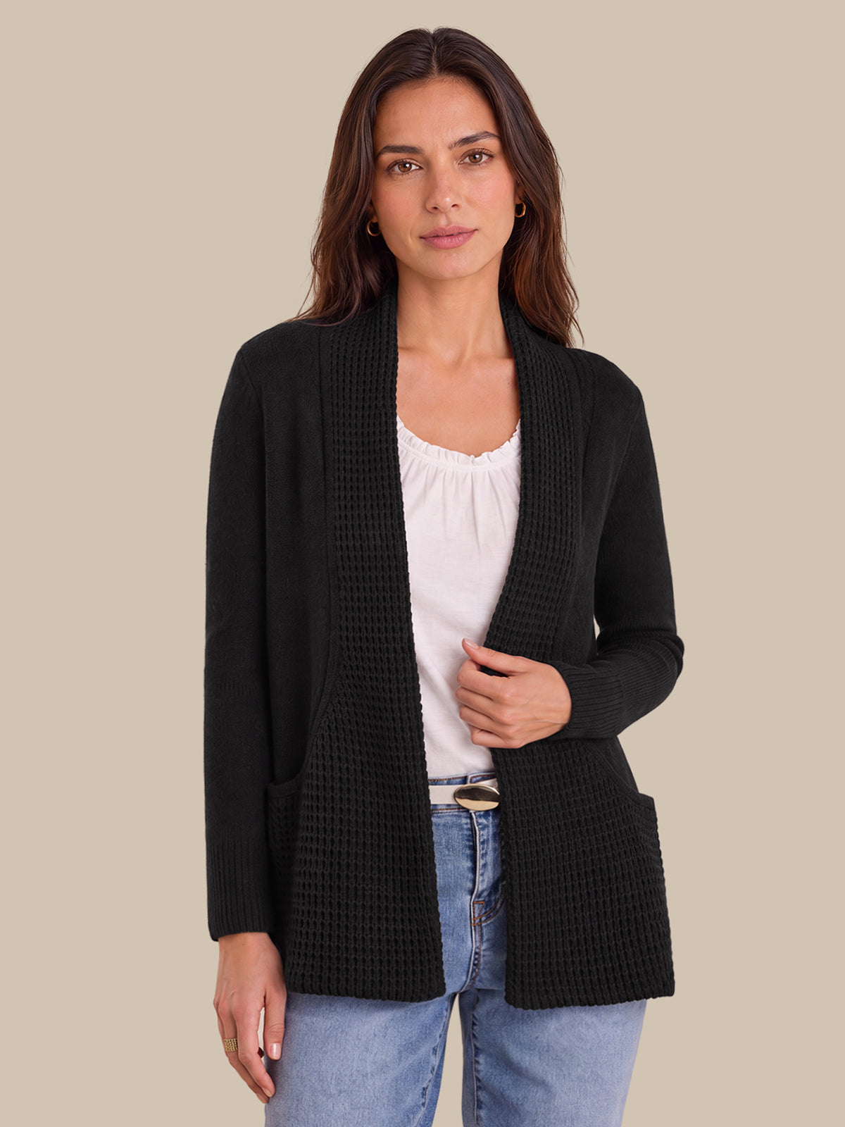 A woman modeling a black textured open-front cardigan over a white top and blue jeans, set against a solid beige background.