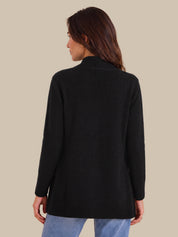A woman shown from the back wearing a black long-sleeve knit sweater and light blue jeans against a solid beige background.