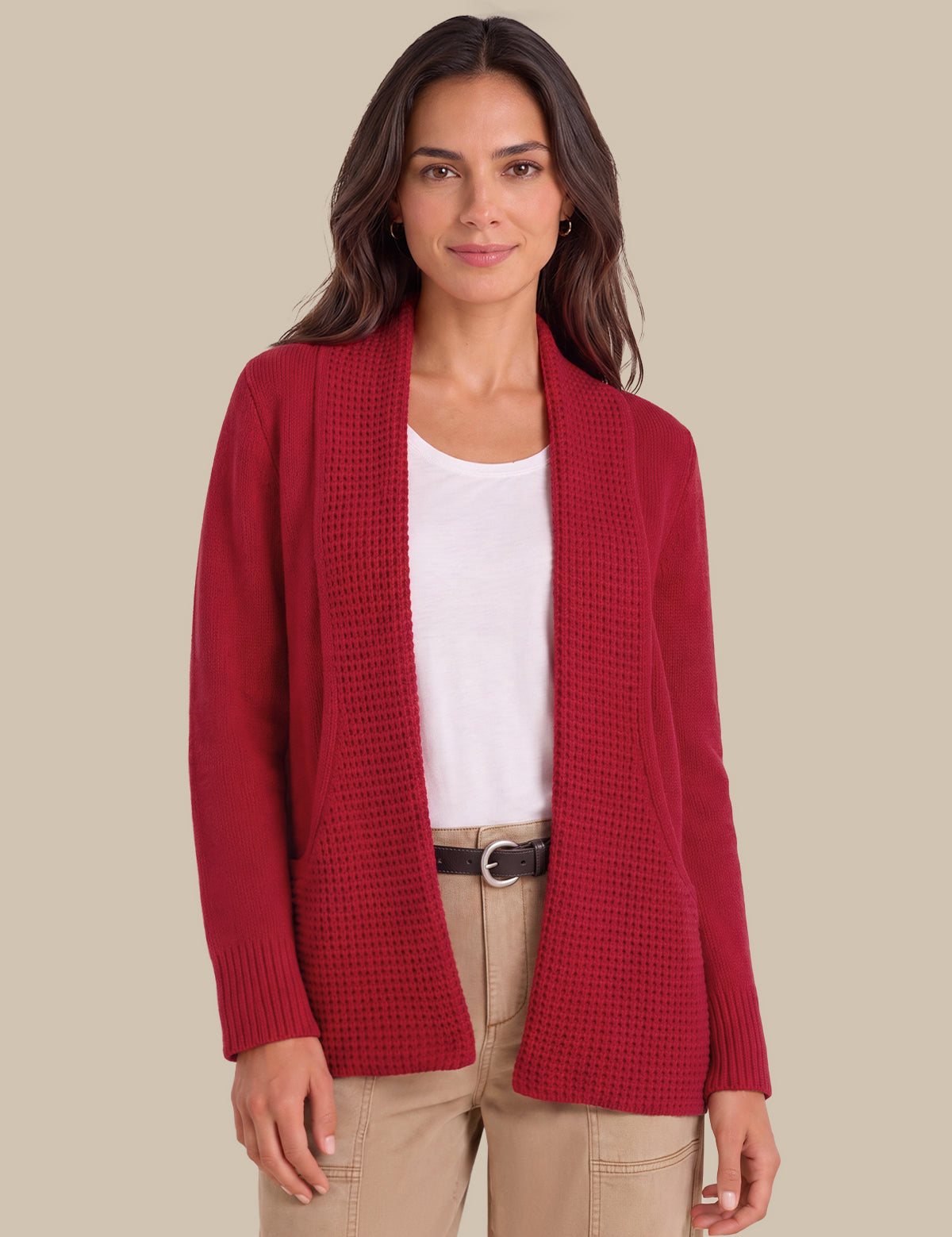 A woman modeling a red waffle-knit open-front cardigan over a white top and beige pants, set against a solid beige background.