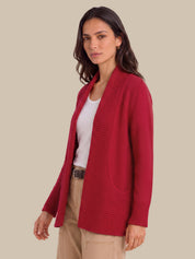 A woman modeling a red open-front knit cardigan over a white top and beige pants, photographed against a plain warm beige studio background.