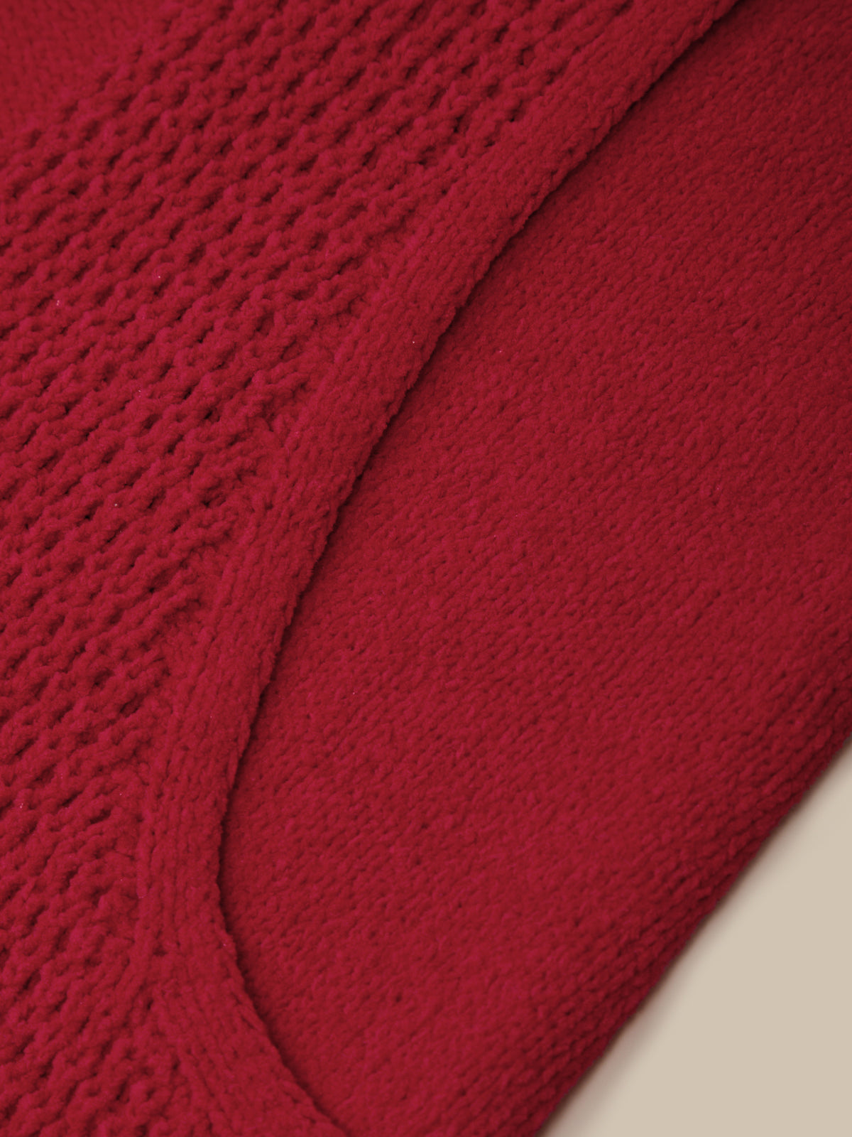 Close-up of a red knit fabric with a textured openwork pattern and a smooth curved seam, shown against a light neutral background.