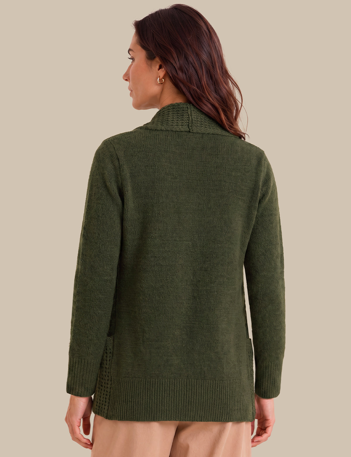 A woman shown from the back wearing an olive green knit sweater with textured knit details on the shoulders and hem, paired with beige pants, against a solid beige background.