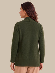 A woman shown from the back wearing an olive green knit sweater with textured knit details on the shoulders and hem, paired with beige pants, against a solid beige background.