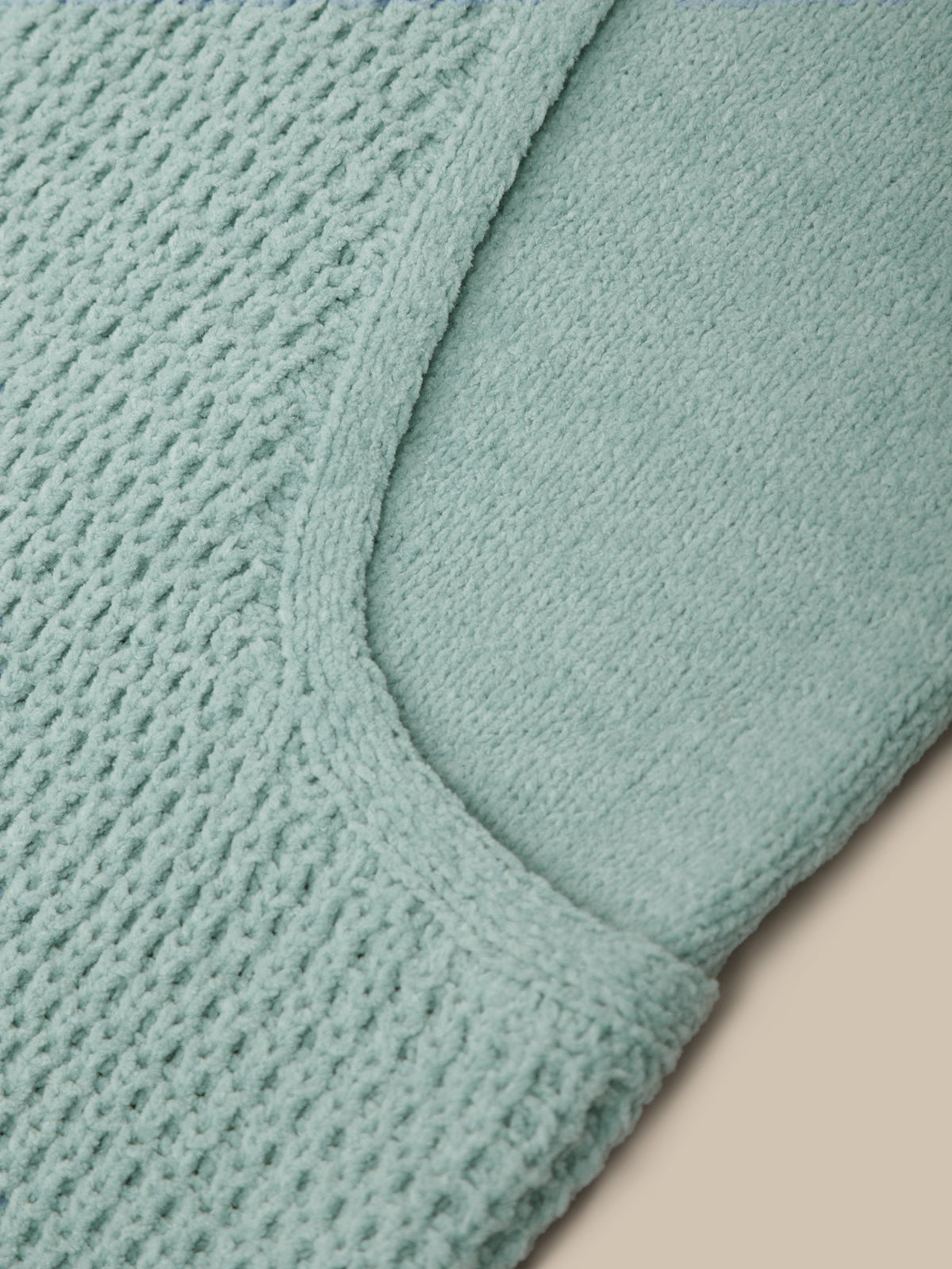 Close-up of a mint green knit fabric with a waffle texture and a curved seam, shown against a light beige background.