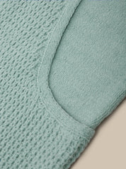 Close-up of a mint green knit fabric with a waffle texture and a curved seam, shown against a light beige background.