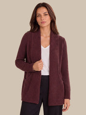 A woman modeling a textured, open-front cardigan in a deep burgundy color, worn over a white top and dark pinstriped trousers, set against a solid beige background.