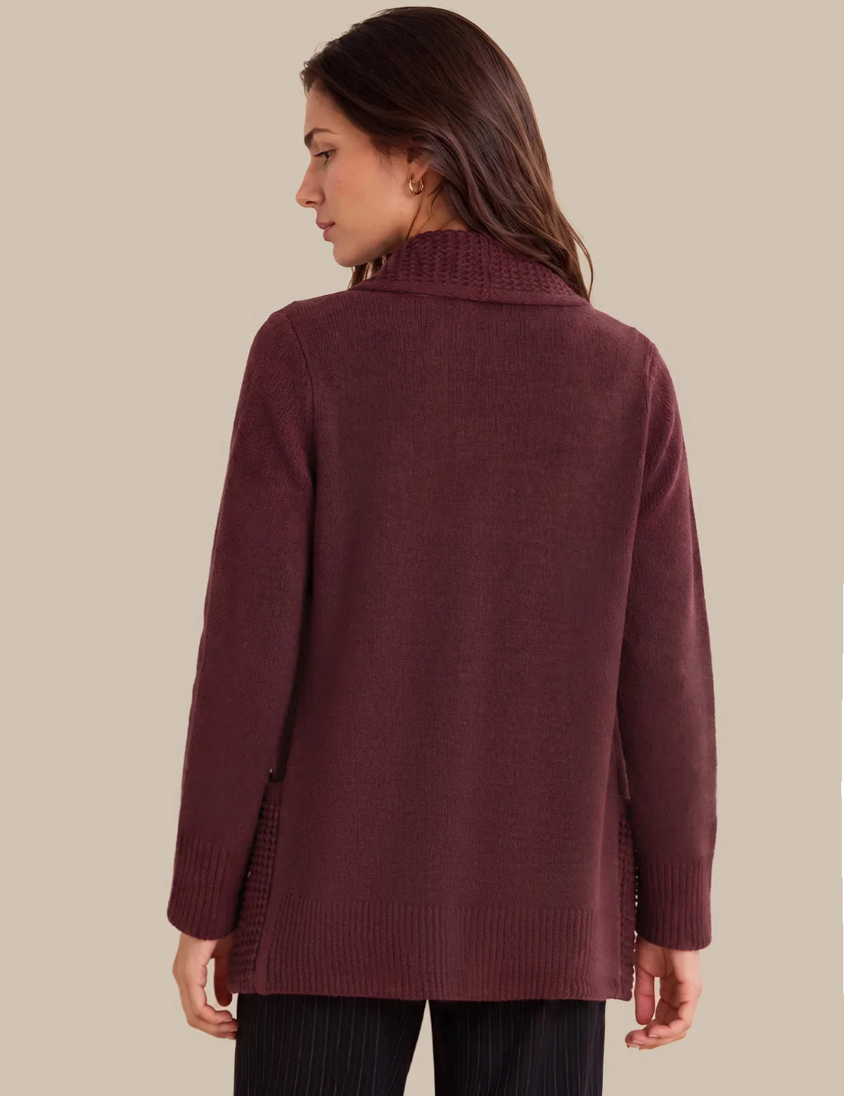 A woman shown from the back wearing a long-sleeve knit sweater in a deep burgundy or maroon color, paired with dark pinstriped pants, against a solid beige background.