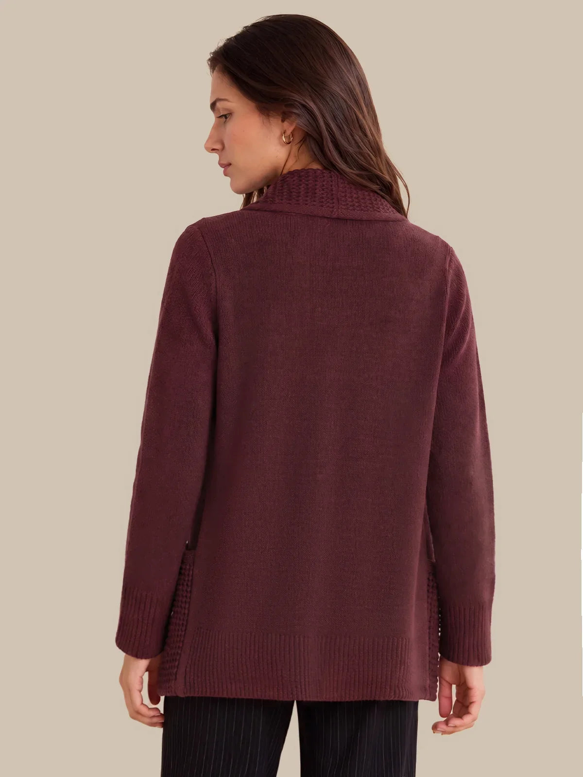 A woman shown from the back wearing a long-sleeve knit sweater in a deep burgundy or maroon color, paired with dark pinstriped pants, against a solid beige background.
