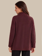 A woman shown from the back wearing a long-sleeve knit sweater in a deep burgundy or maroon color, paired with dark pinstriped pants, against a solid beige background.